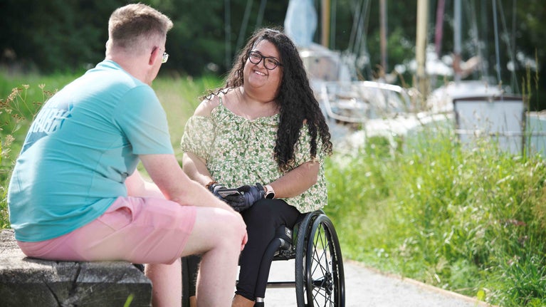A visitor who uses a wheelchair, and their partner, stopping for a break along the accessible path.